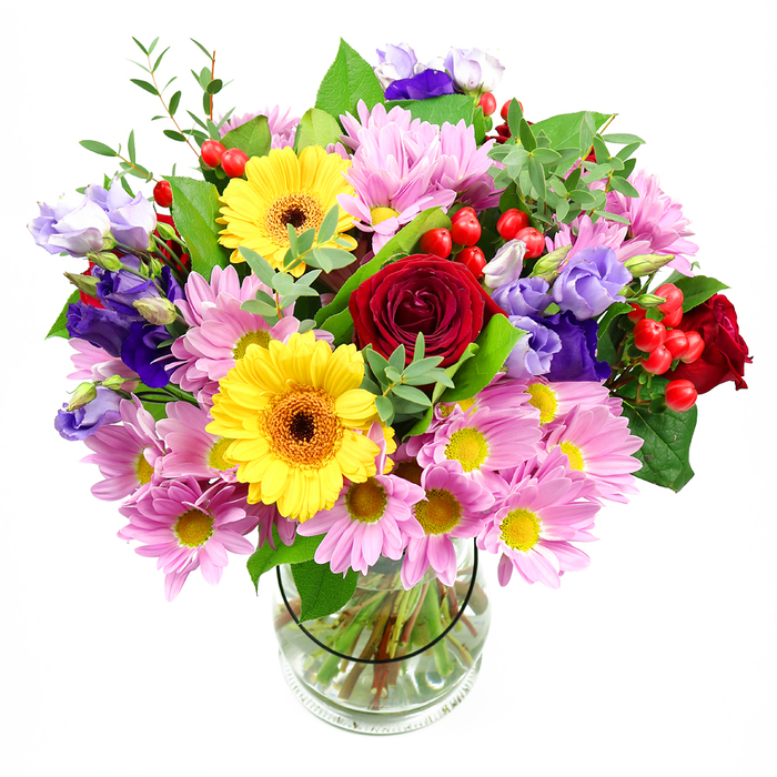 A lush, mixed-flower arrangement stands elegantly in a clear glass vase, the bouquet captured against a smooth white background so the colours appear vivid and bright. The central focus is a cluster of deep red roses, their velvety petals layered in spirals that suggest both depth and tenderness, like a quiet, heartfelt conversation shared at a kitchen table in Crofton Park. Surrounding these, sunny yellow gerbera daisies with dark brown-orange centres create bold, circular bursts of colour, their petals fanning out like rays of sunlight, instantly lifting the mood as if the light had shifted over nearby Brockley and Ladywell Cemeteries' green spaces. Around this vivid core, generous clusters of pink daisies or chrysanthemums spread outward, their slender, slightly curved petals forming soft ruffles that add volume and a comforting, familiar feel. Woven among these blooms are elegant lisianthus in shades of purple and lavender, their bell-shaped forms and slightly ruffled edges introducing a gentle sophistication and cool contrast that keeps the palette from feeling too warm. Bright red hypericum berries appear at intervals, each round and glossy, providing a distinct textural counterpoint to the softness of the petals. A layered mix of foliage frames the flowers-deep green, broad leaves creating structure, while lighter, more delicate sprigs and tendrils lend movement and a sense of natural ease, like stems gathered from local gardens near Ewhurst Road. The transparent vase reveals straight, carefully trimmed stems positioned in fresh, clear water, adding to the sense of freshness and professional arrangement. Altogether, this bouquet conveys warmth, joy, and celebration, making it perfectly suited for marking milestones, saying thank you, or simply adding a bright, floral accent to a Crofton Park home.